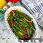 green beans and sweet peppers with bits of garlic on serving plate with parsley garnish