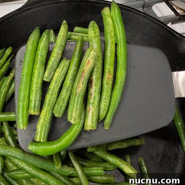 green beans on black spatula above pan showing brown blister/burn marks on beans
