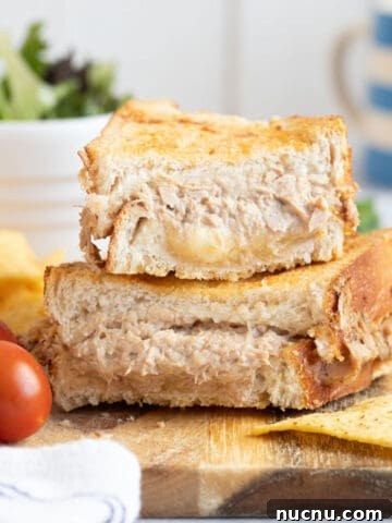 Air fryer tuna mwlt sandwich on a wooden board with salad and crisps.