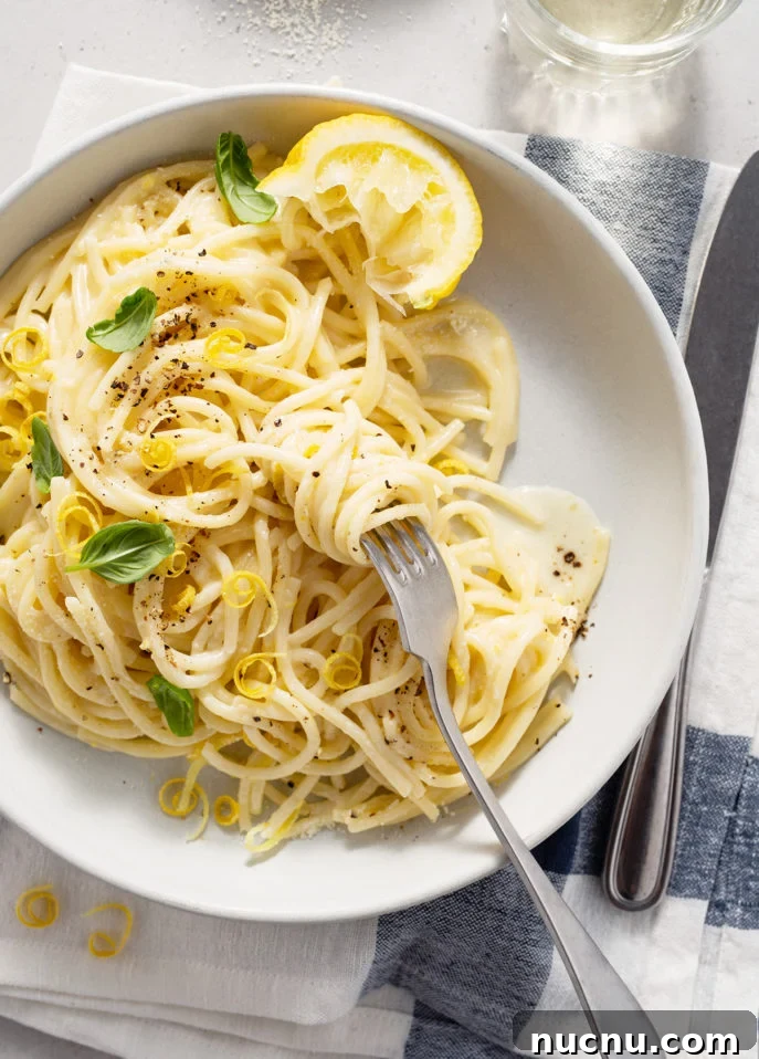 A plate of spaghetti al limone topped with lemon zest, black pepper, and basil leaves