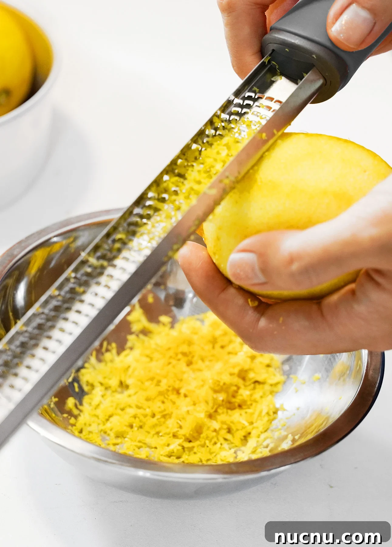Creamy Lemon Spaghetti Recipe: Zesty, Silky Pasta in 20 Minutes 6 A person grating the yellow zest from a lemon over a metal bowl