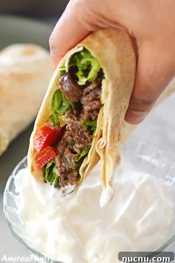 a hand holding beef shawarma wrap dipping it in garlic shawarma dip