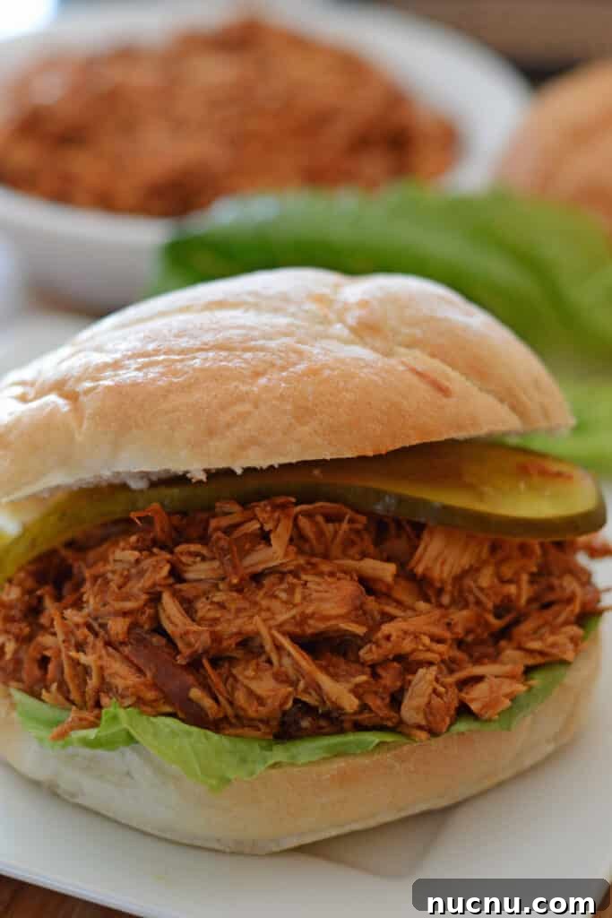 pulled chicken sandwich on a white plate with lettuce leaves in the back