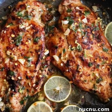 lemon garlic chicken in a black colored pan garnished with fresh lemon slices.