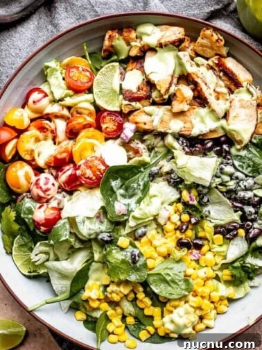 chicken strips, corn, tomatoes, and black beans set over salad greens in a salad bowl and drizzled with avocado salad dressing