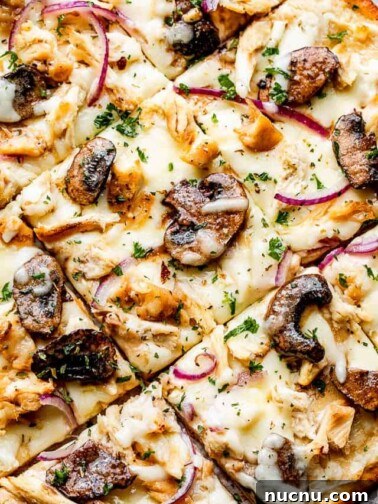 top view of a grilled pizza topped with Cheese, mushrooms, chicken, and red onions