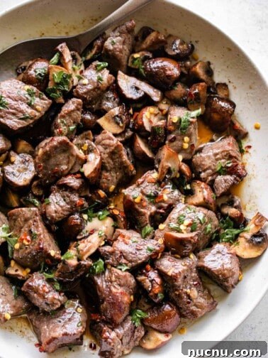 up close shot of air fryer steak bites and mushrooms served in a round white serving platter.