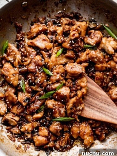 wooden spoon stirring through bourbon chicken while cooking in a stainless steel skillet.