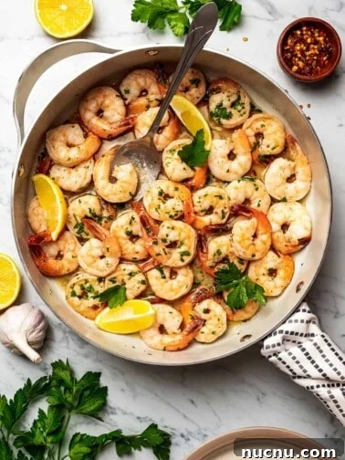 Shrimp scampi in a skillet, with a big spoon placed inside to spoon out shrimp.