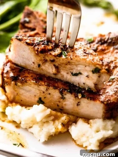 fork stabbing through a halved pork chop set on a bed of mashed potatoes