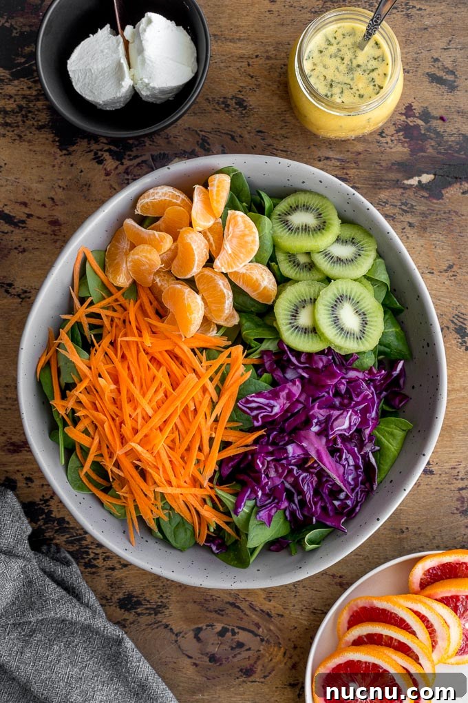 Winter Citrus Salad with Honey Dressing and Toasted Almonds 6 Ingredients to make Winter Salad arranged in a large bowl next to a jar of dressing and goat cheese.