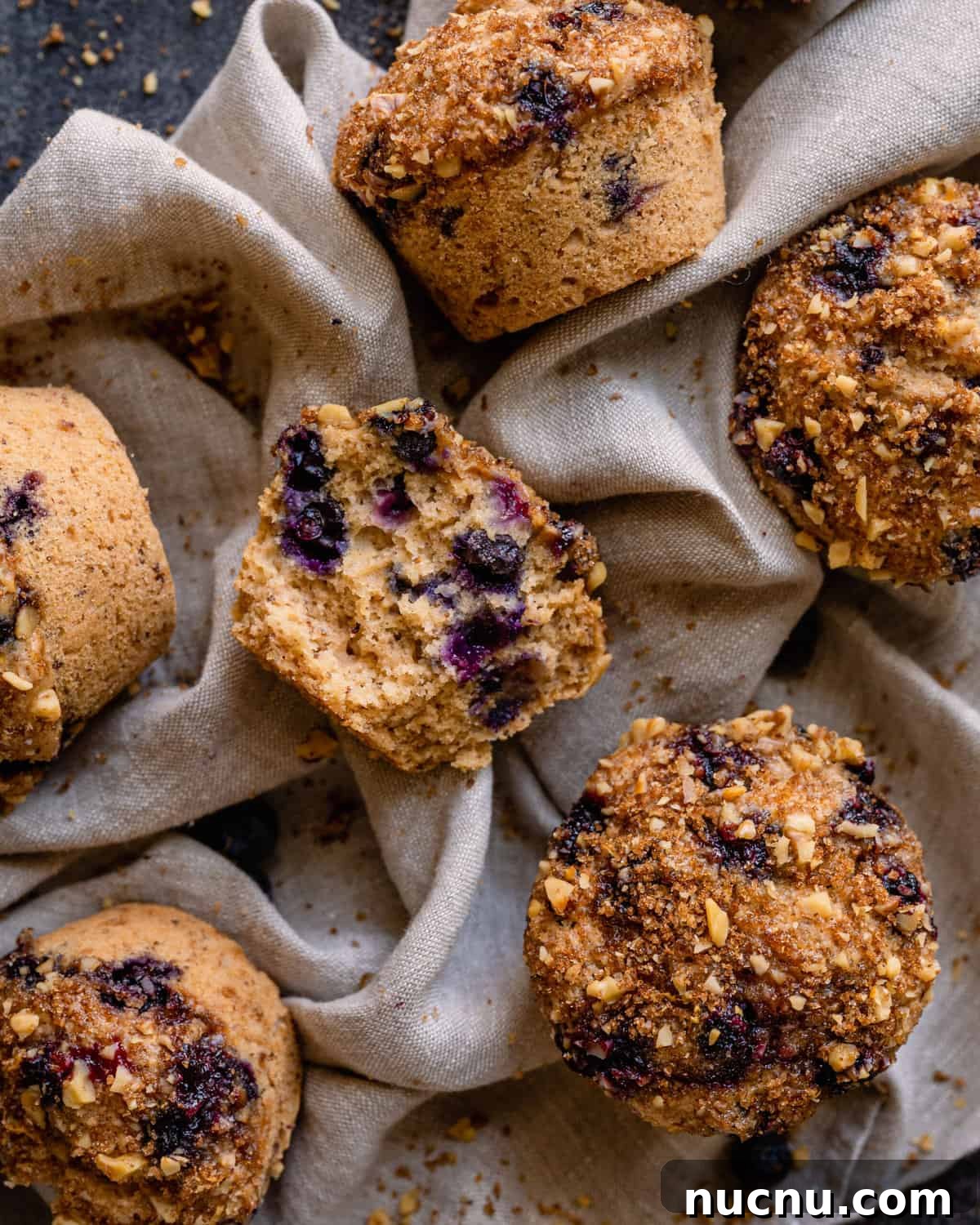 Vegan Blueberry Muffins Recipe: Moist, Fluffy, Simple to Make 14 flatlay of vegan blueberry muffins on linen with middle muffin sliced open to show texture.