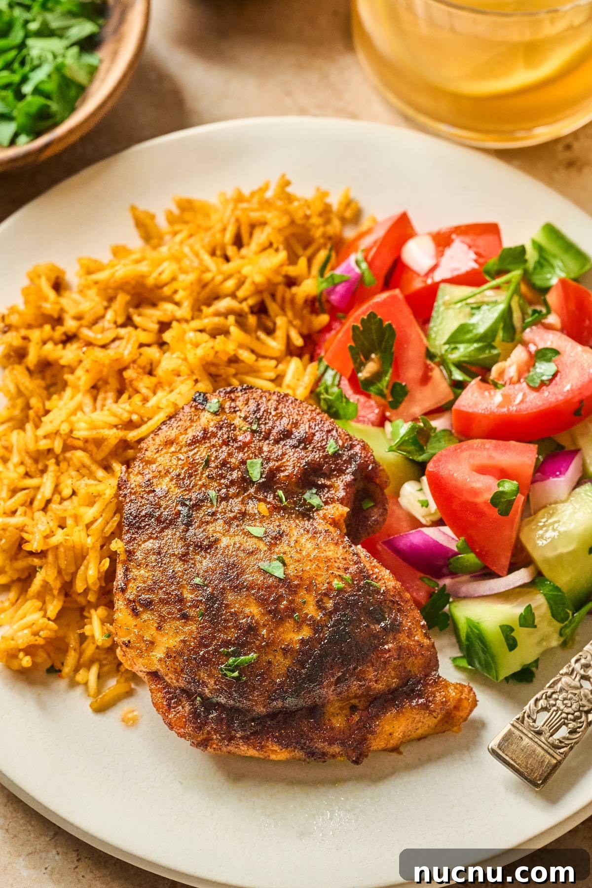 One-Pan Shawarma Chicken and Rice Skillet Recipe 11 A plate with spiced chicken, yellow rice, and a fresh salad of tomatoes, cucumbers, and red onions.