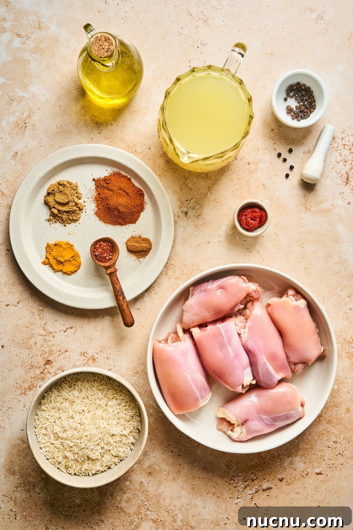 One-Pan Shawarma Chicken and Rice Skillet Recipe 14 Raw chicken thighs, spices, rice, olive oil, broth, tomato paste, and peppercorns on a light countertop.