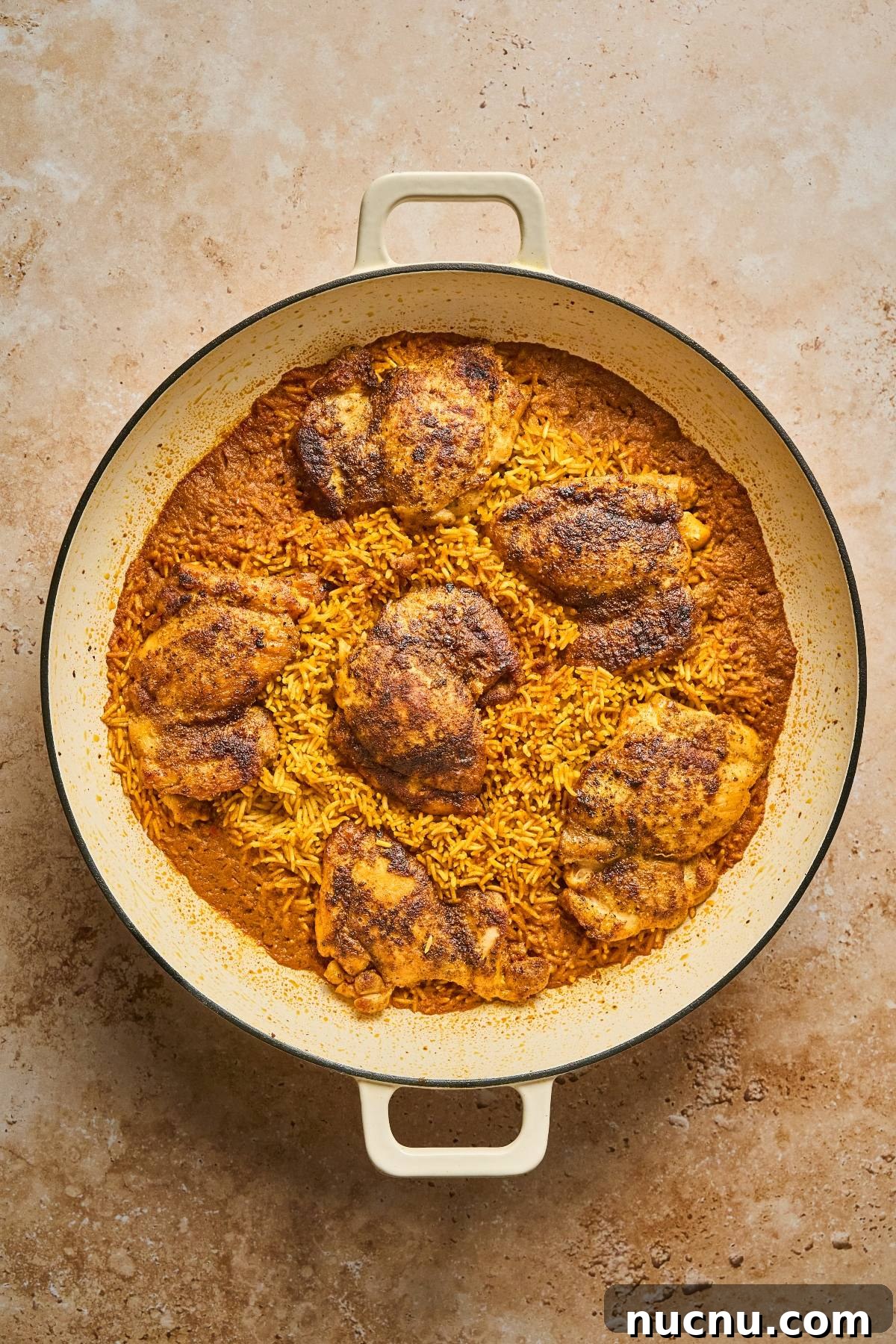 One-Pan Shawarma Chicken and Rice Skillet Recipe 19 A round pan with baked seasoned chicken thighs on top of golden rice.