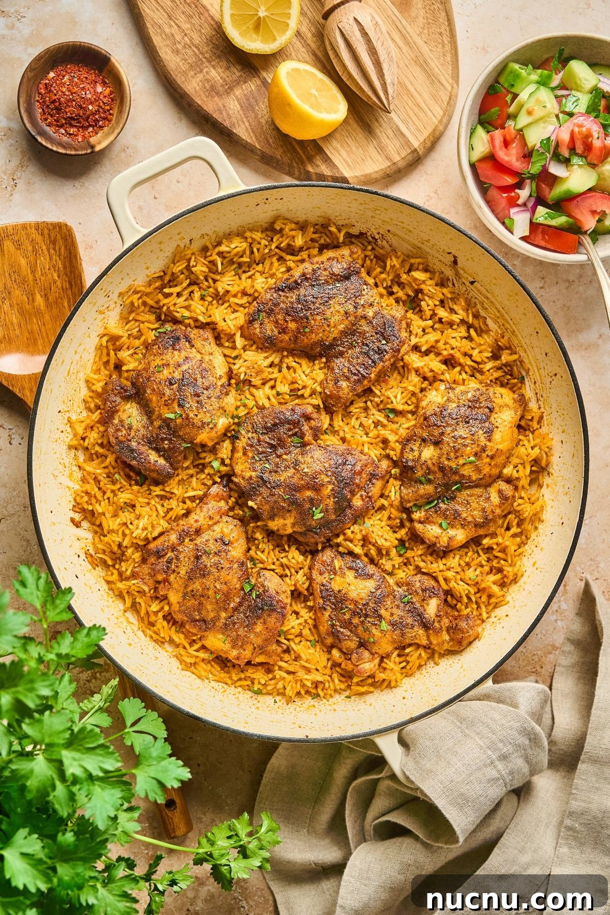 One-Pan Shawarma Chicken and Rice Skillet Recipe 8 A pan of seasoned chicken thighs on yellow rice, with salad, lemon, and spices on the side.