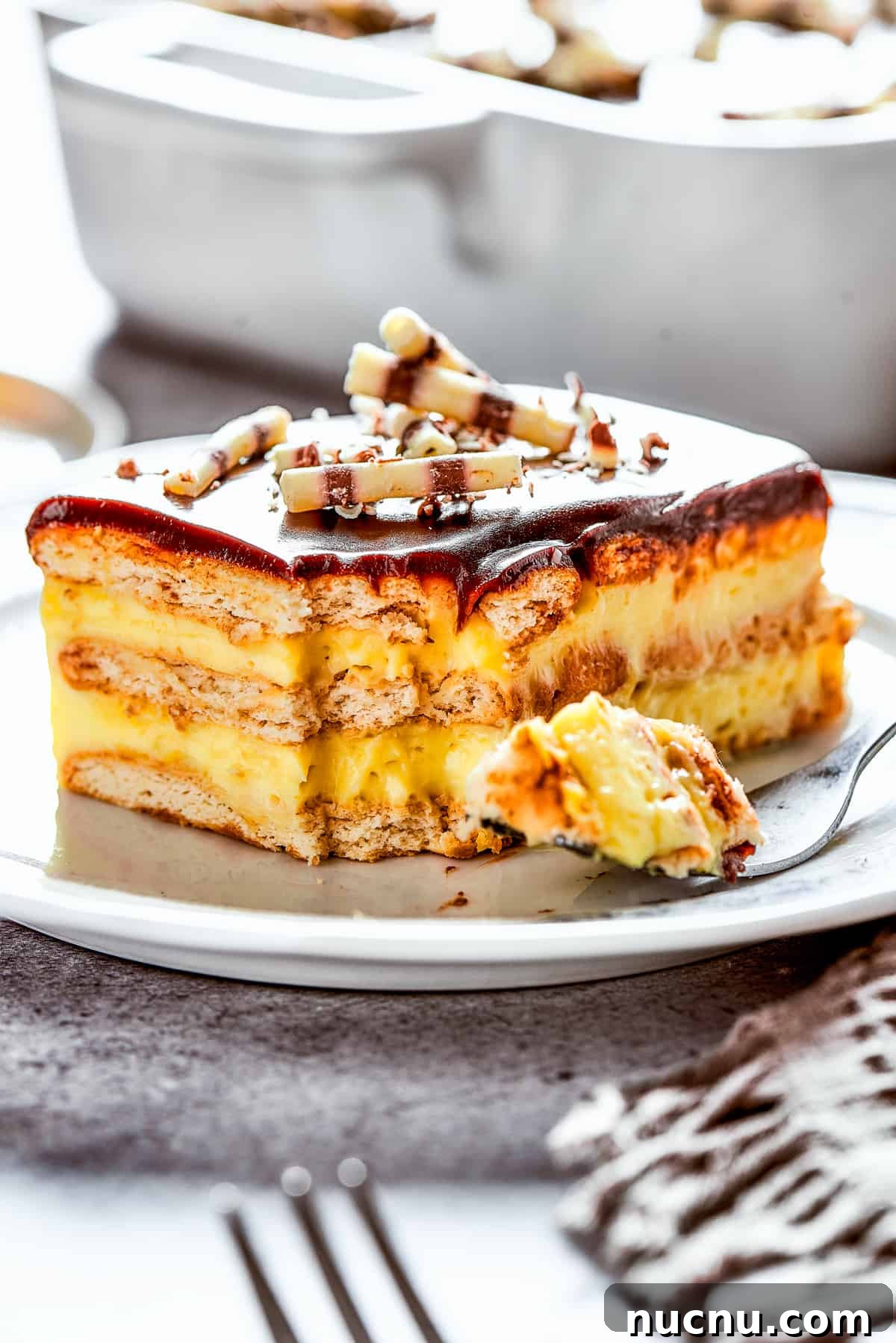 Chocolate eclair cake is loaded with creamy and smooth pudding, decadent chocolate ganache, and tender cookies, and it's so easy to make. A slice of chocolate eclair cake on a plate, with a fork on the plate with a bite of cake.