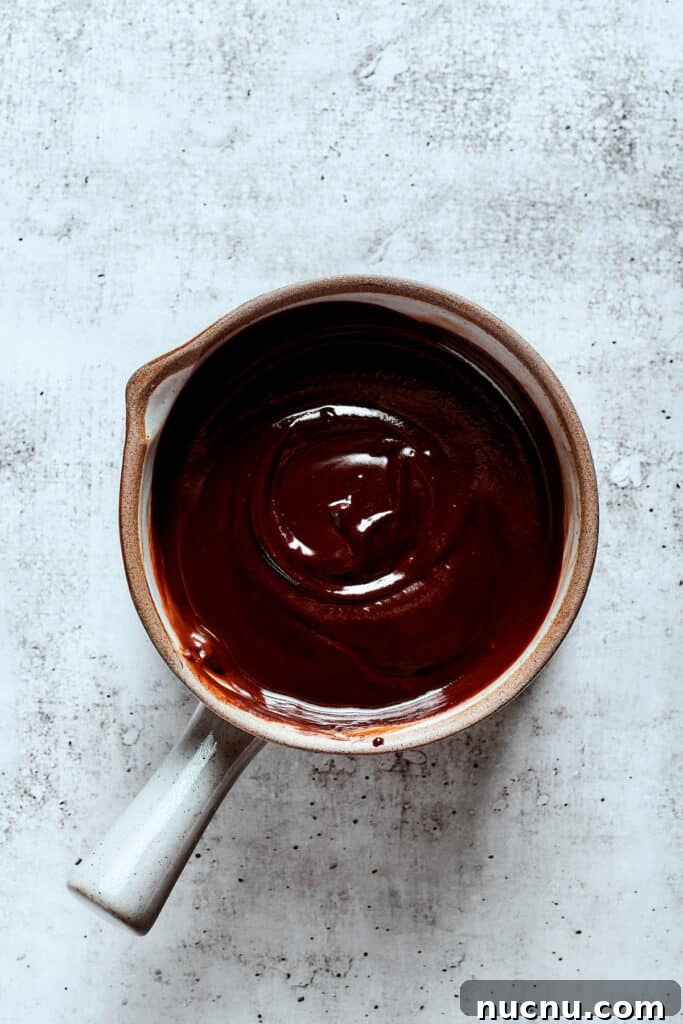 Chocolate eclair cake is loaded with creamy and smooth pudding, decadent chocolate ganache, and tender cookies, and it's so easy to make. Overhead view of a saucepan full of chocolate ganache.
