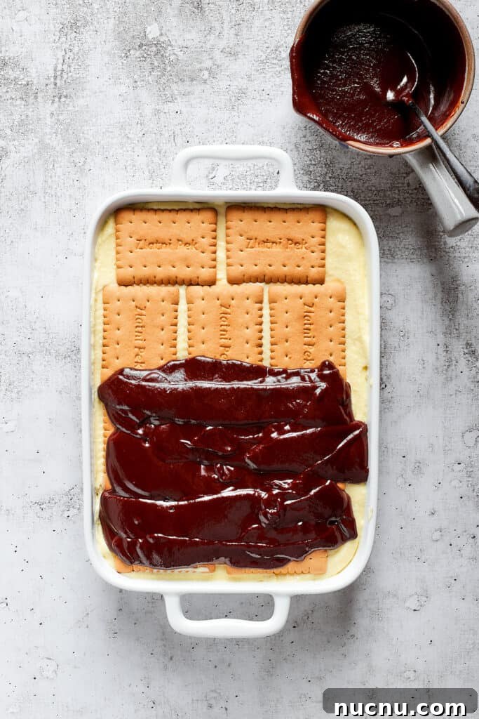 Decadent Chocolate Éclair Cake Recipe for Dessert Lovers 2 Overhead view of chocolate ganache half-spread over cookies in a baking dish.