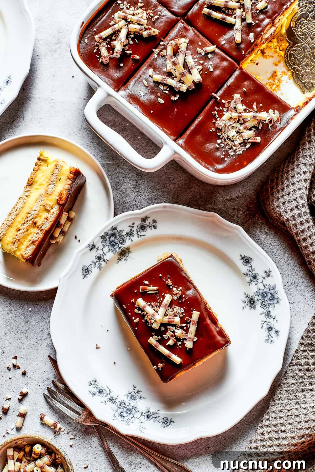 Chocolate eclair cake is loaded with creamy and smooth pudding, decadent chocolate ganache, and tender cookies, and it's so easy to make. Overhead shot of chocolate eclair cake in a baking dish, and a couple of slices of the cake served on dessert plates.