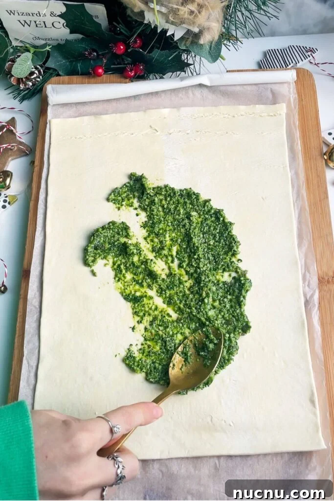 Spooning basil pesto onto a sheet of puff pastry.