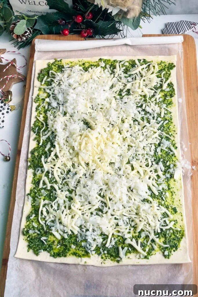 Cheese scattered over pesto on a puff pastry sheet.