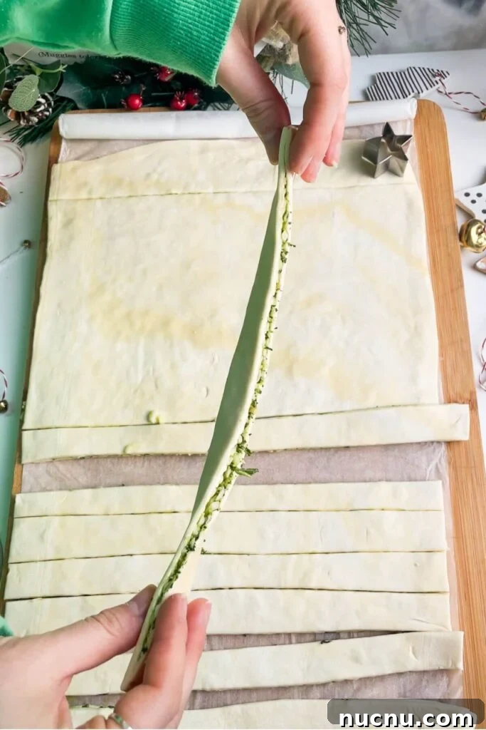 Holding up a strip of puff pastry layered with basil pesto and mozzarella.