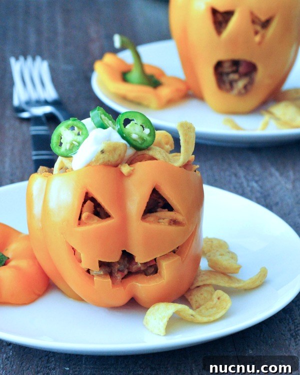 Frito Pie Stuffed Peppers two orange bell peppers carved into a halloween jack o lantern, filled with Frito pie (chili and fritos)