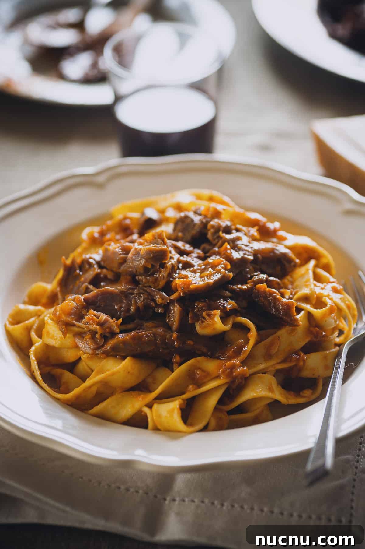a white bowl filled with cooked noodles topped with a meat sauce