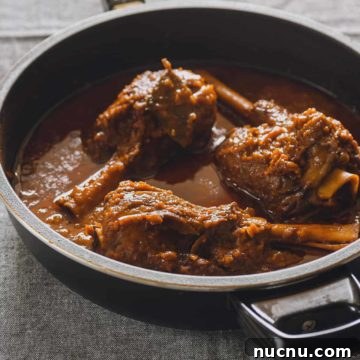 three braised lamb shanks in a black pan