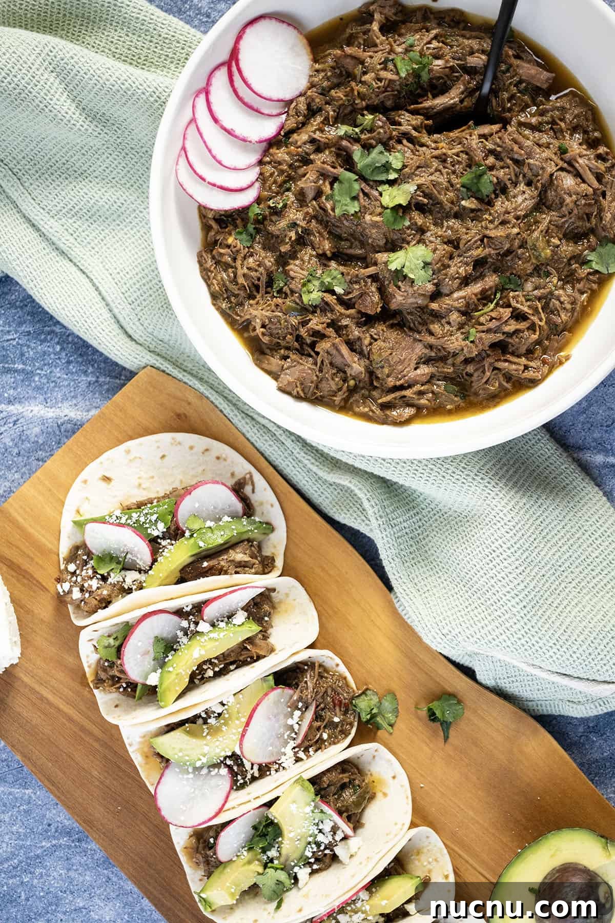Dutch Oven Barbacoa Tacos Recipe — Tender Slow-Cooked Beef Tacos 8 Beef barbacoa in a bowl alongside tacos with sliced radish, avocado, and cotija cheese.