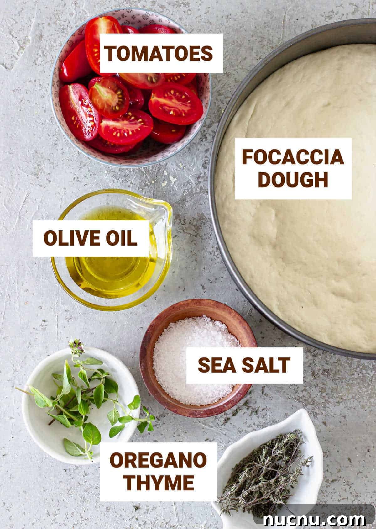 Tomato Focaccia Recipe with Step-by-Step Video Tutorial 4 Grey surface with ingredients for tomato focaccia including dough, oil, salt and herbs