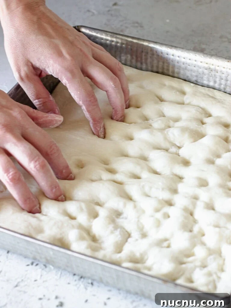 Tomato Focaccia Recipe with Step-by-Step Video Tutorial 5 Hands dimpling focaccia dough in a square light metal baking pan.
