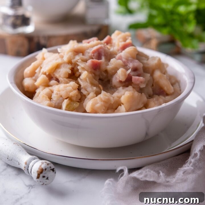 Grandma Browns baked beans in a white bowl atop a white plate. In the background is a second bowl of baked beans.