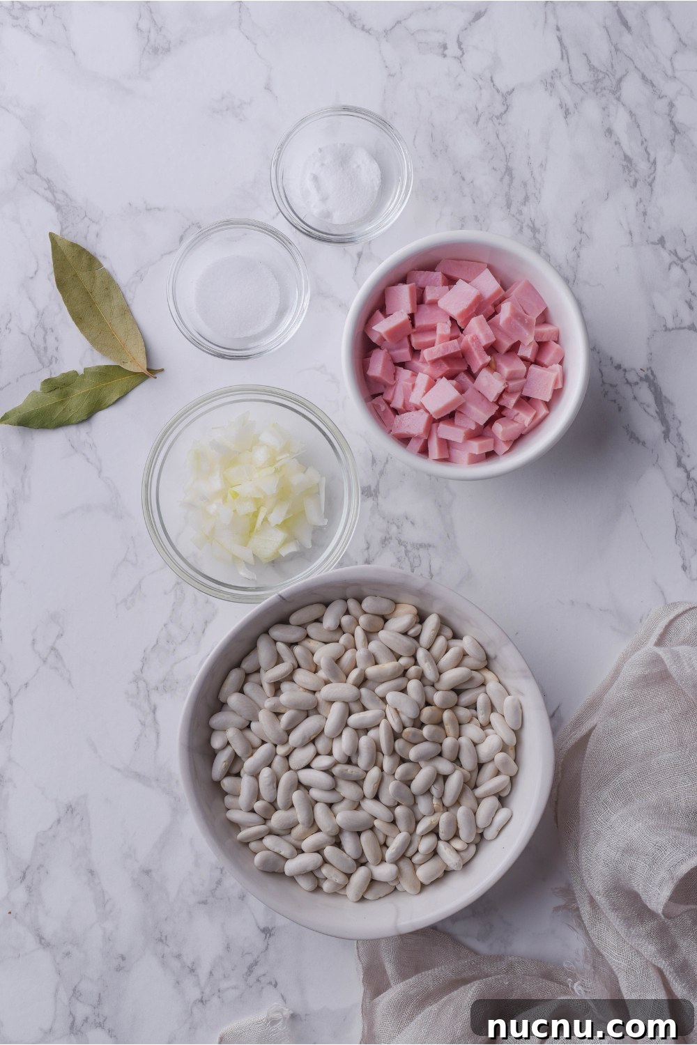 Copycat Grandma Brown's Baked Beans Recipe You’ll Love 4 An assortment of ingredients including bowls of dried beans, cubed ham, diced onion, salt, and two bay leaves.