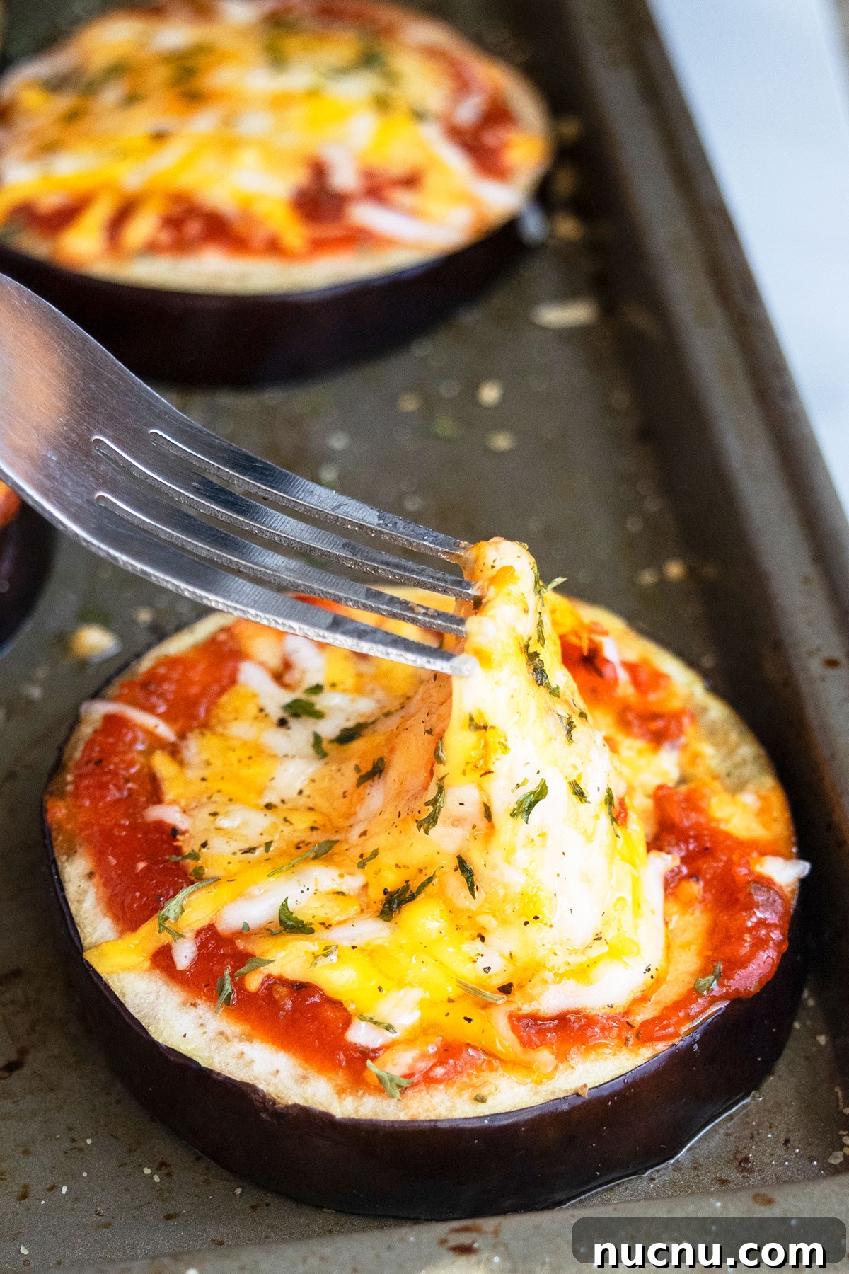 One-Pan Eggplant Pizza Recipe for Quick Weeknight Meals 2 Fork showing a cheese pull on eggplant pizza on baking tray.