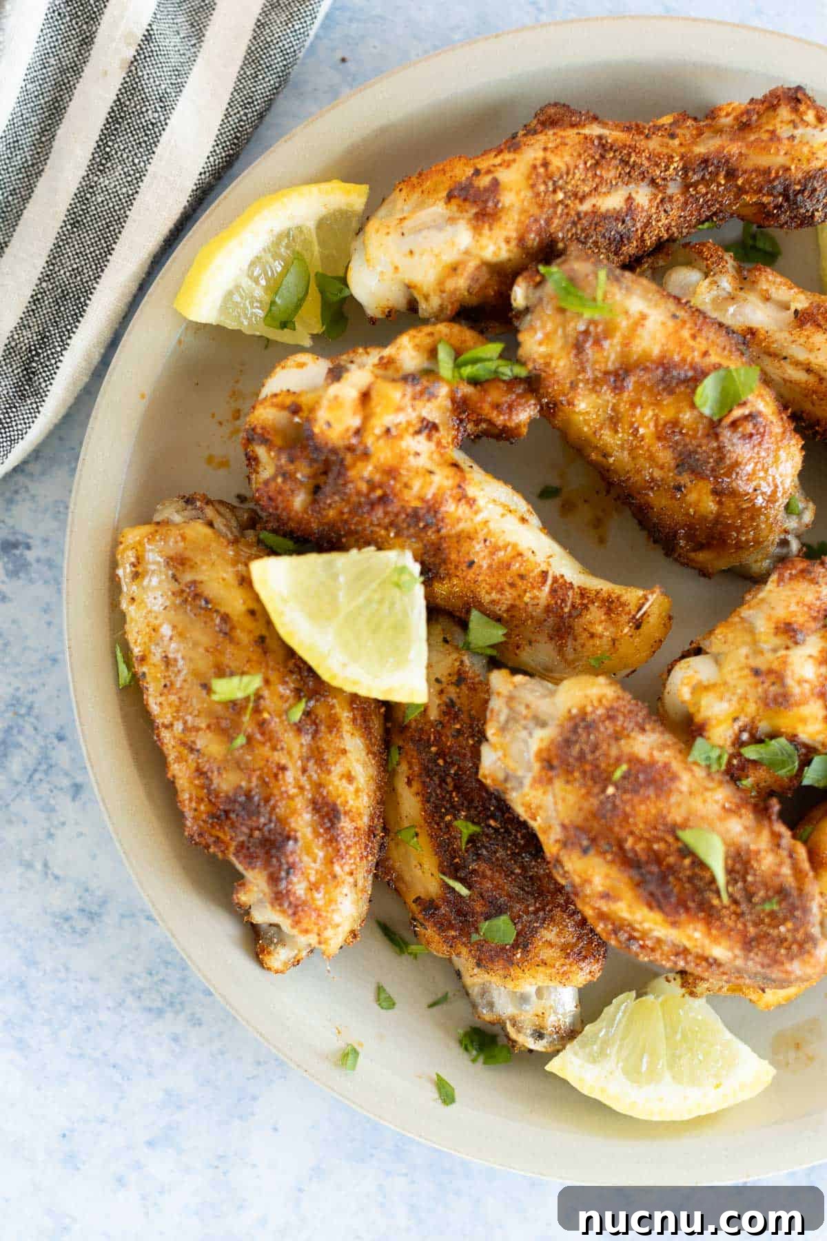 Crispy Dry-Rub Wings Recipe for Perfectly Spiced Chicken 2 A plate of dry rub chicken wings garnished with lime wedges and chopped parsley, served on a light-colored plate.