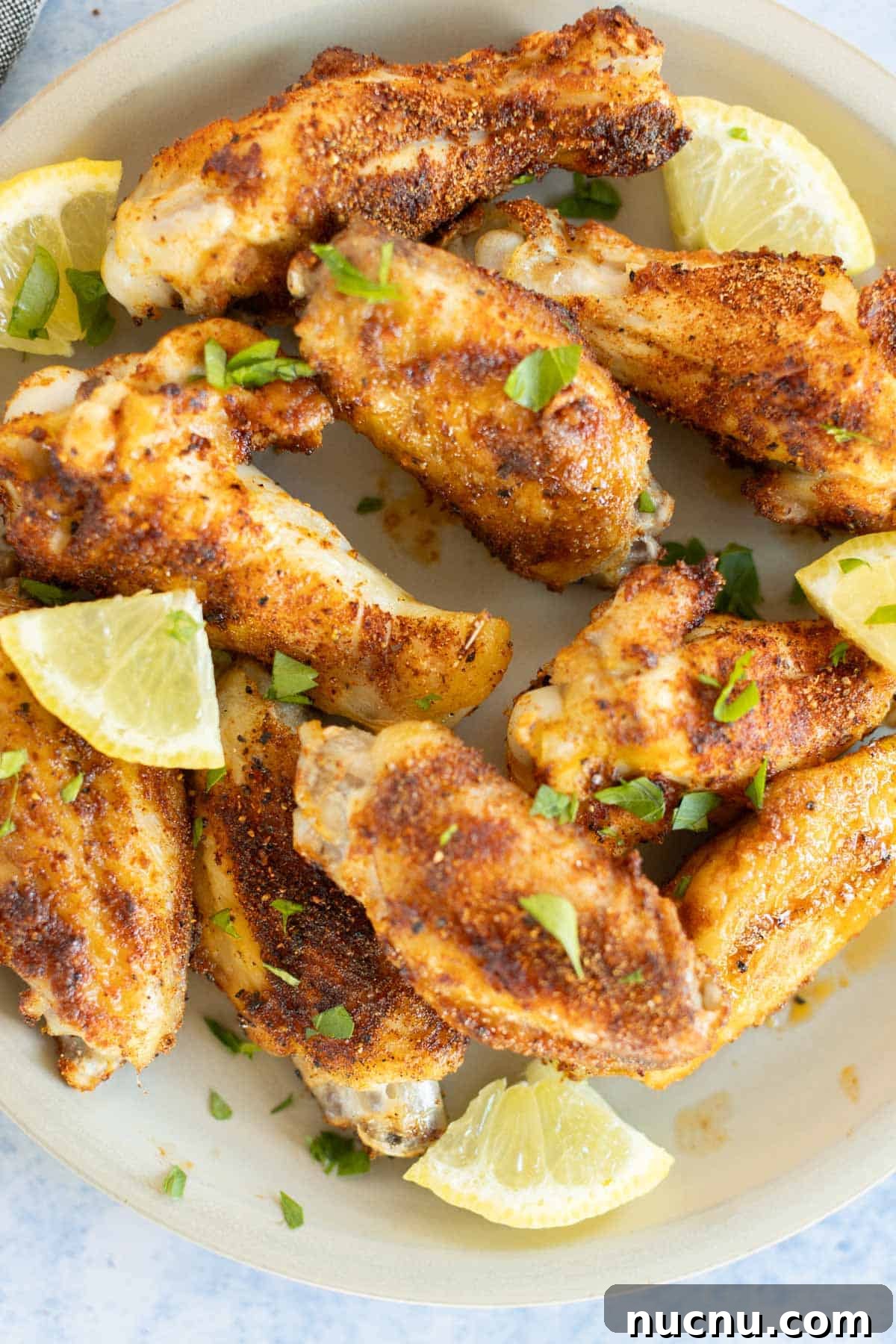 Crispy Dry-Rub Wings Recipe for Perfectly Spiced Chicken 12 Plate of dry rub chicken drumsticks garnished with lime wedges and chopped parsley, viewed from above.