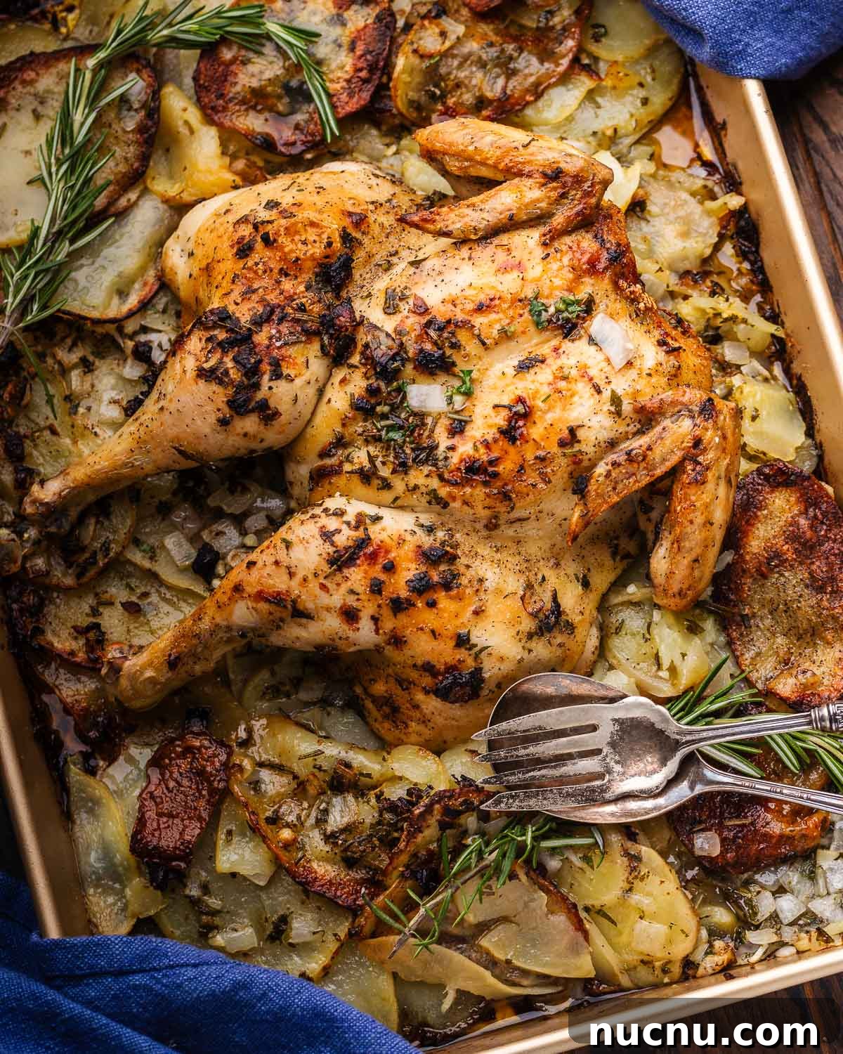 Spatchcock chicken and potatoes on baking sheet with fork and spoon.