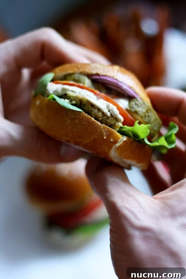 Juicy vegan falafel burger in a pretzel bun served with creamy tahini sauce and crispy and tender sweet potato fries. The best healthy falafel burger I've ever had!