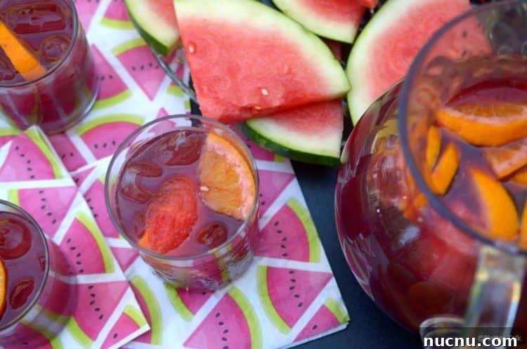 Three glasses of red wine vodka sangria with full pitcher, garnished with melon.