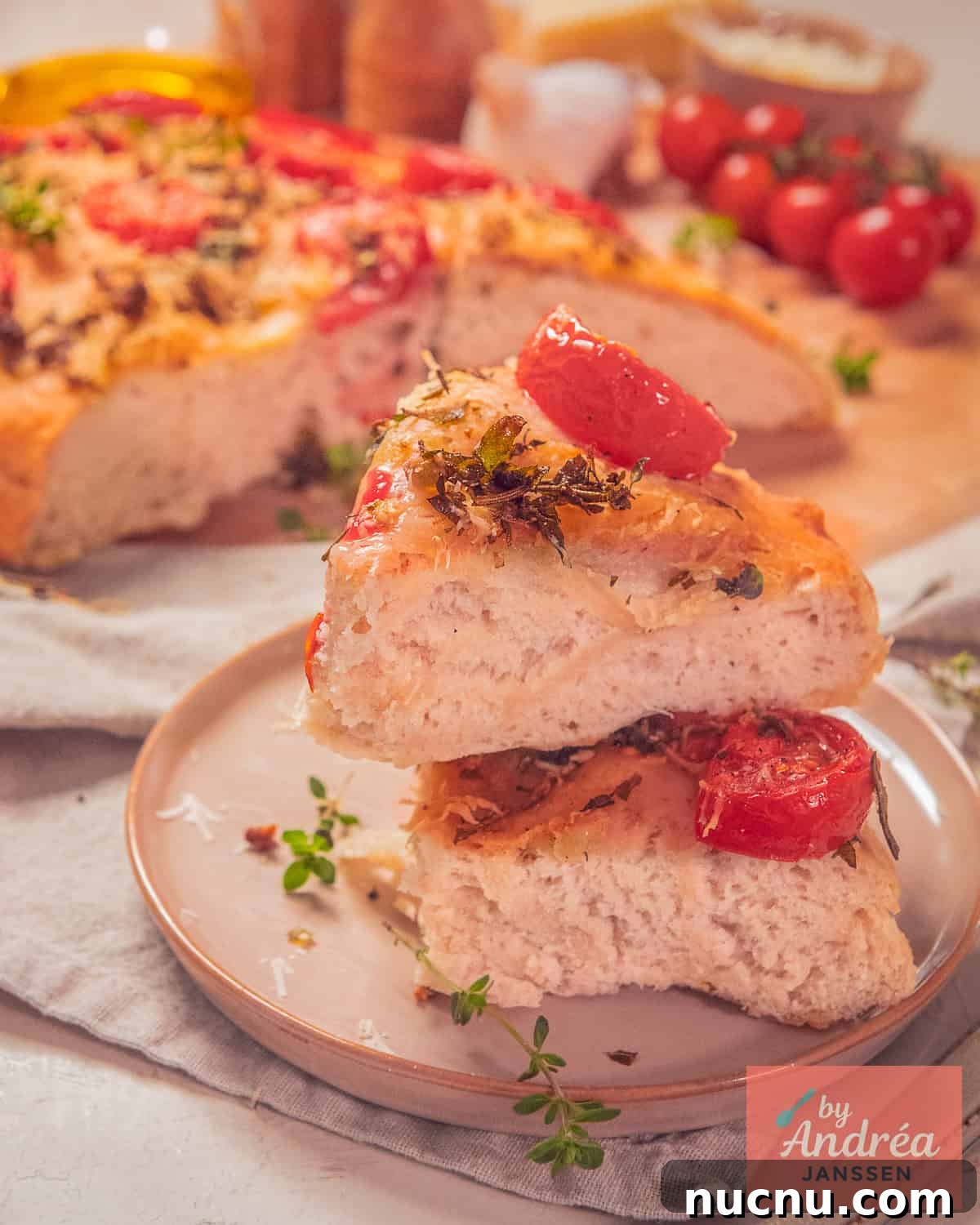 Crispy-Edged Tomato Focaccia with Parmesan and Olive Oil 8 Two pieces of focaccia stacked on top of each other. The focaccia is topped with herbs, tomato, and Parmesan cheese.