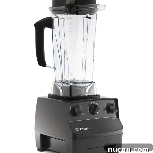 A black Vitamix blender with a clear plastic pitcher, black lid, and handle, featuring control dials and switches on the front of the base.