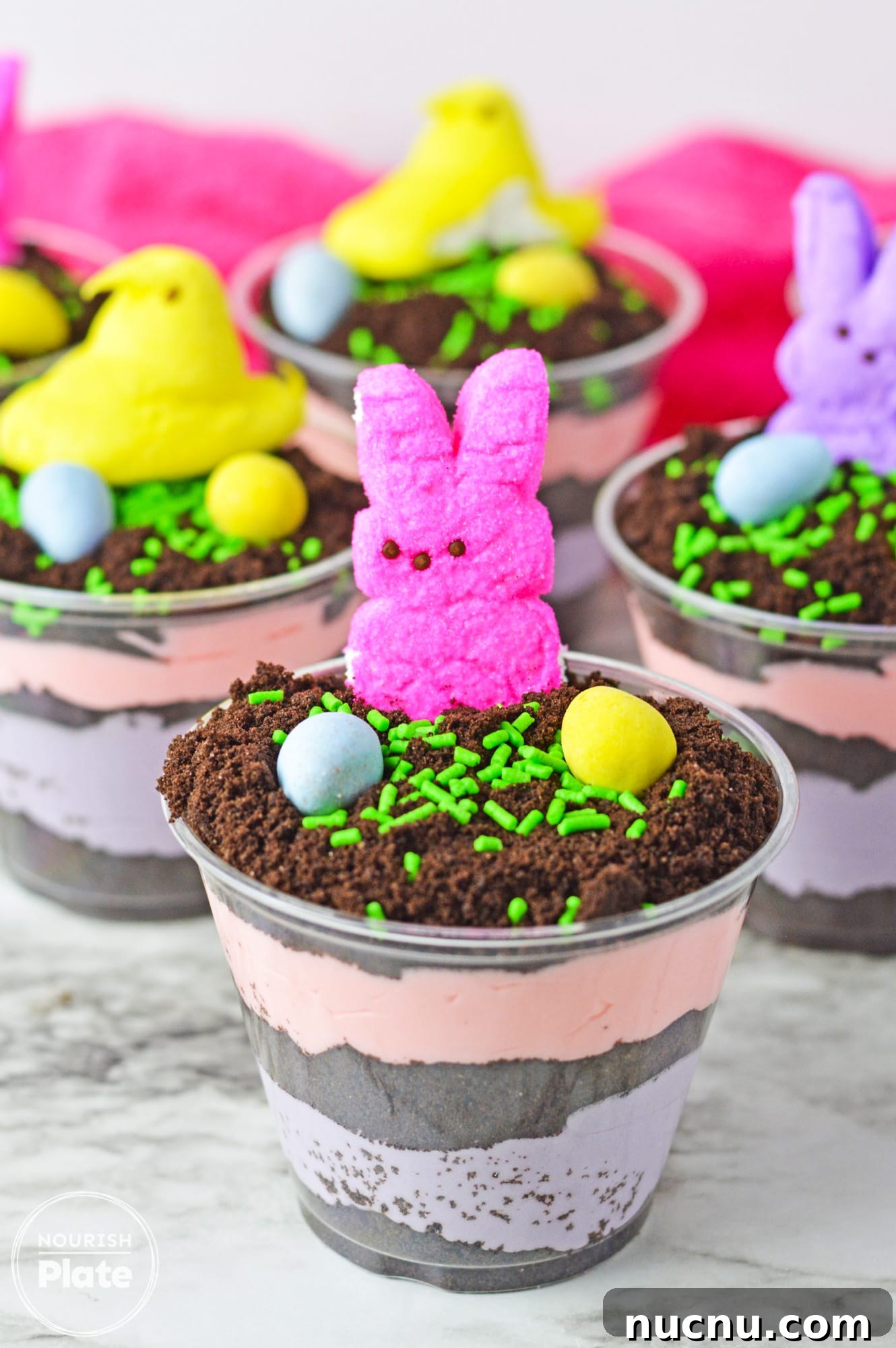 Easter Dirt Cup Desserts: Chocolate Pudding Treats with Candy Eggs 2 Easter dirt cups with layered instant pudding in colors, topped with peeps and mini eggs.