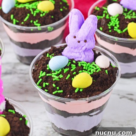 Easter Dirt Cup Desserts: Chocolate Pudding Treats with Candy Eggs 6 Easter dirt cups with layered instant pudding in colors, topped with peeps and mini eggs.