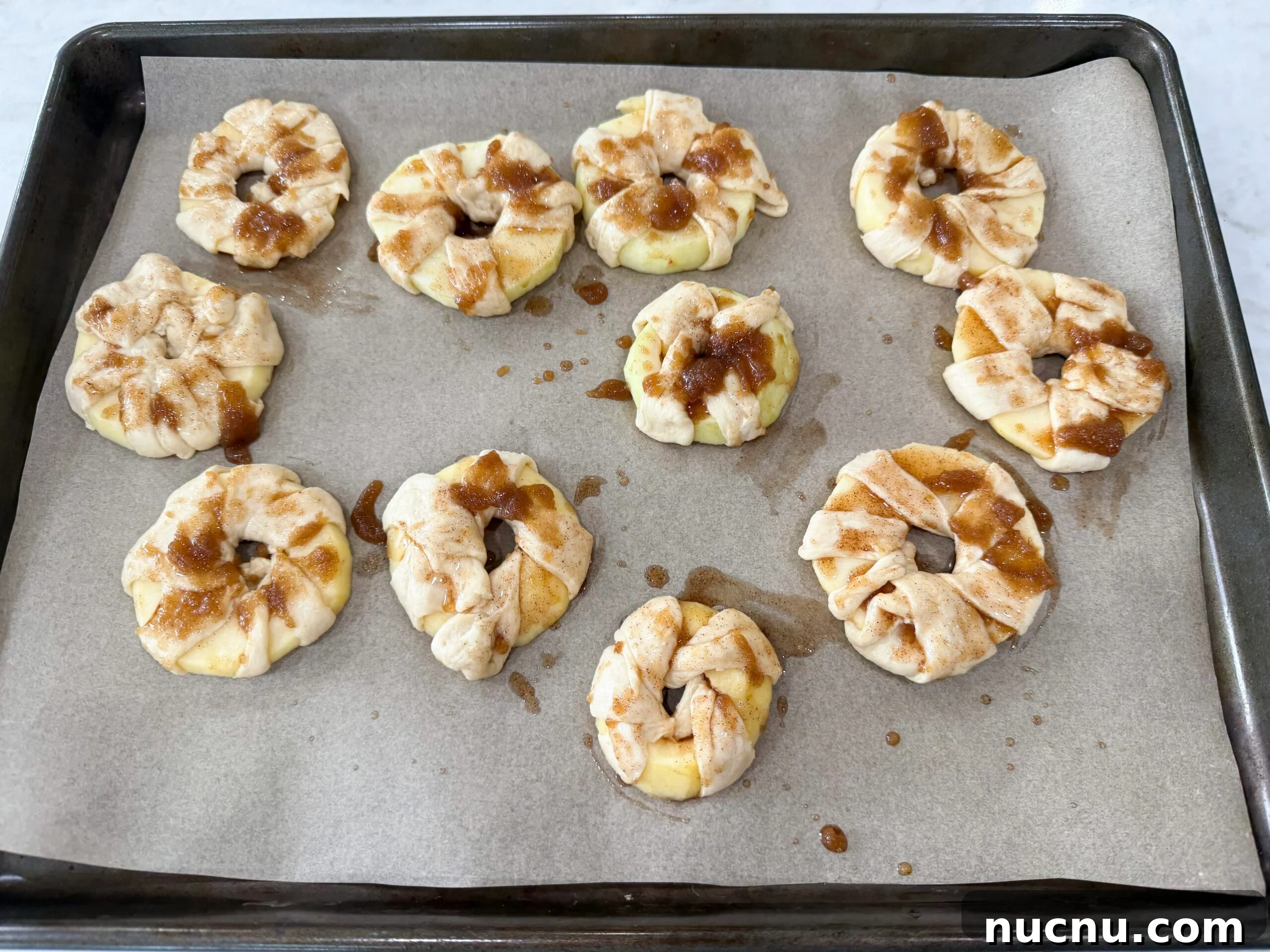 Brushing cinnamon sugar butter on wrapped apple donuts before baking