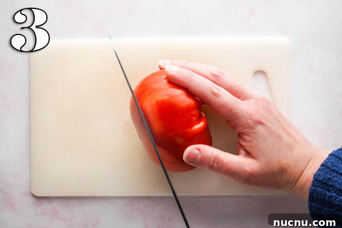 Caprese Chicken Sandwich with Fresh Mozzarella & Basil 6 knife cutting a slice off a tomato being held on a cutting board