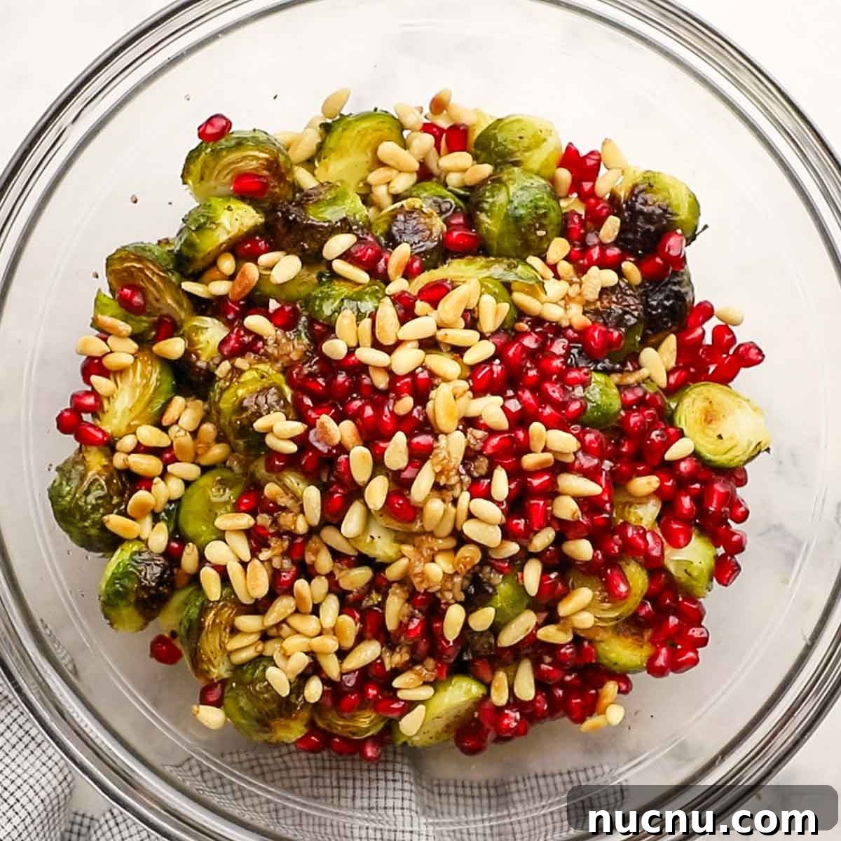 Brussels sprouts in a bowl with pomegranate seeds, pine nuts, and vinaigrette.