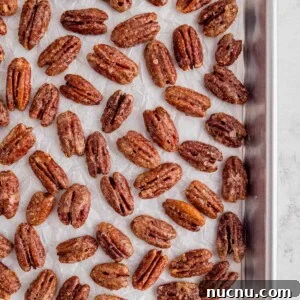 Sweet and Sticky Candied Pecans Recipe for Holiday Gifts 7 candied pecans on a piece of white parchment paper on a baking sheet
