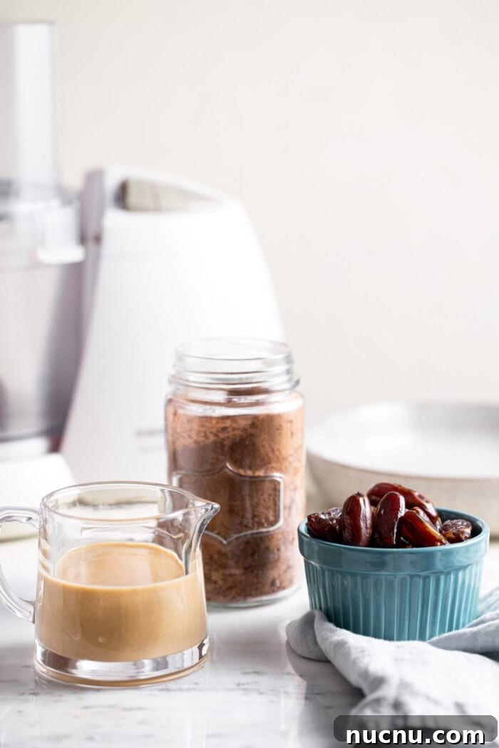 Essential Vegan Pantry Staples for Everyday Cooking 2 Containers of tahini, cacao powder and dates sitting in front of a food processor.
